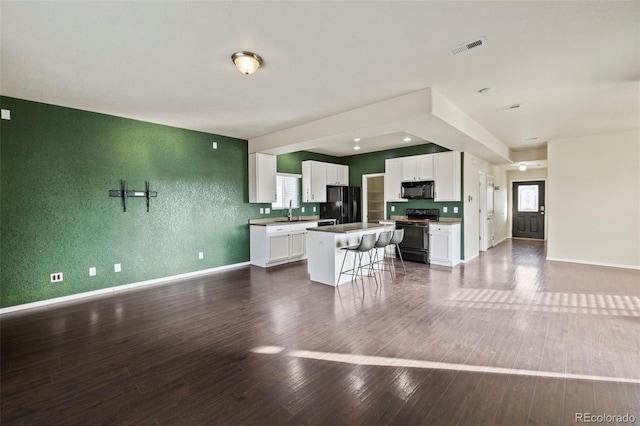 kitchen featuring a kitchen island, white cabinetry, open floor plan, black appliances, and a kitchen bar