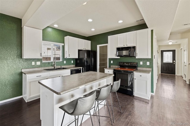 kitchen featuring white cabinets, a center island, black appliances, a kitchen bar, and a sink