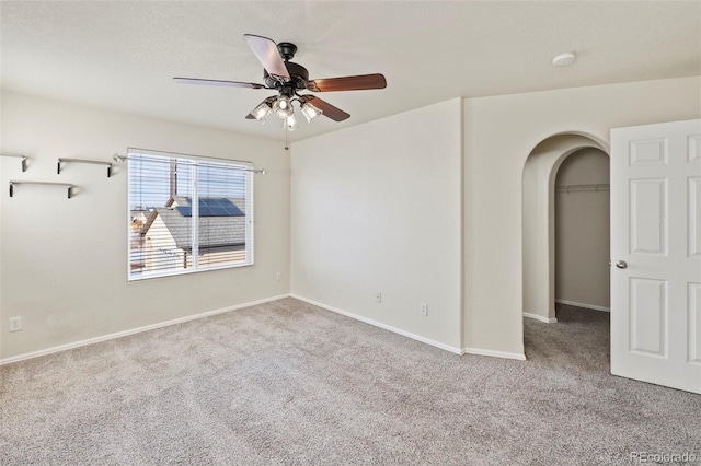 unfurnished room with baseboards, arched walkways, a ceiling fan, and light colored carpet