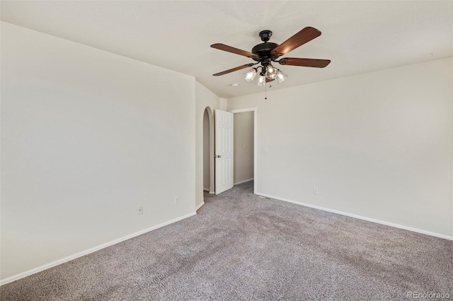 carpeted empty room with baseboards, arched walkways, and a ceiling fan