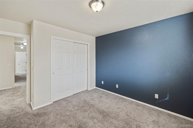 unfurnished bedroom featuring a textured ceiling, a closet, baseboards, and carpet flooring