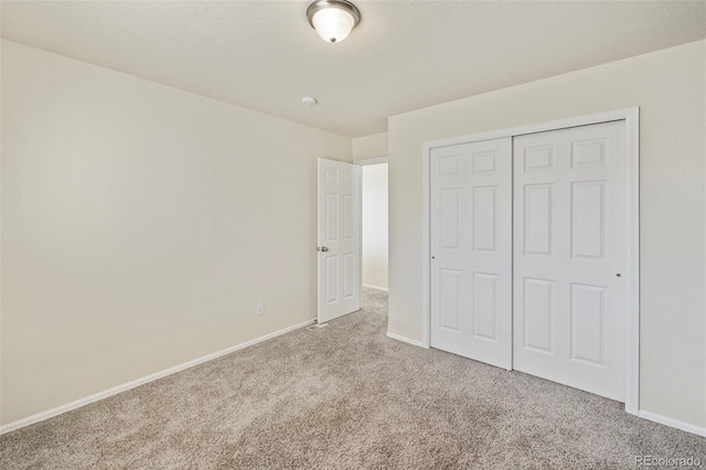 unfurnished bedroom with a closet, light colored carpet, a textured ceiling, and baseboards