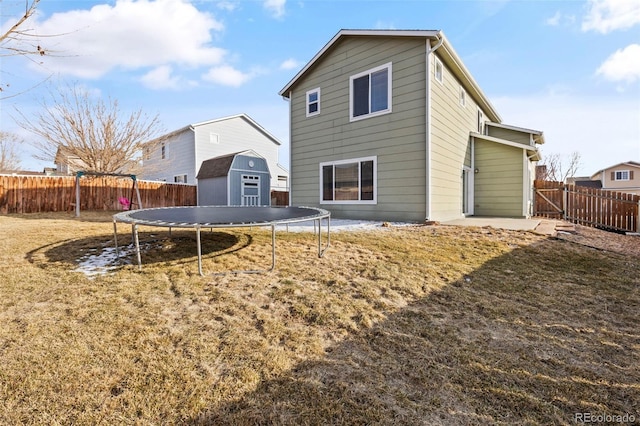 back of house featuring an outbuilding, a fenced backyard, a lawn, a storage unit, and a trampoline