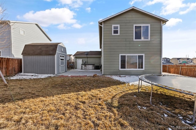 rear view of house featuring a trampoline, an outbuilding, a fenced backyard, and a storage shed