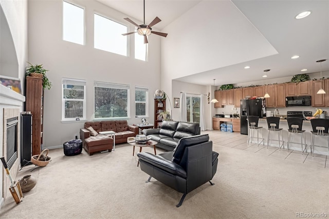 living room featuring ceiling fan, a towering ceiling, light carpet, and a tile fireplace