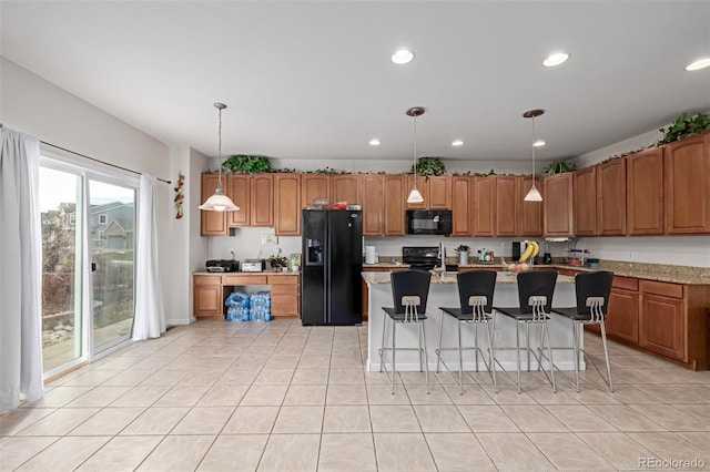 kitchen with a kitchen island with sink, black appliances, a kitchen breakfast bar, hanging light fixtures, and light tile patterned flooring