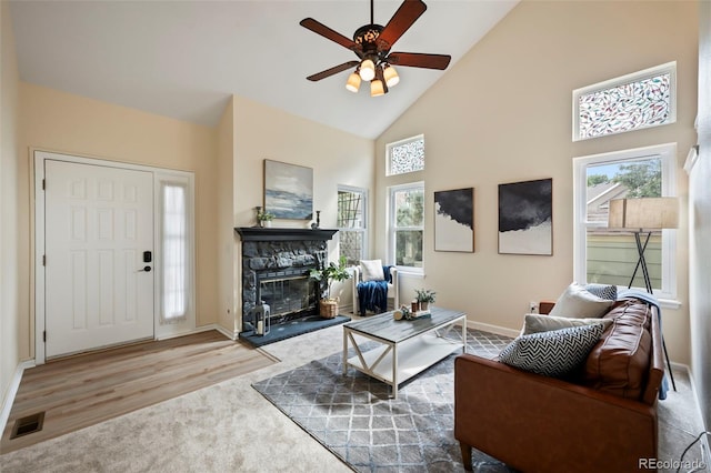 living room featuring a healthy amount of sunlight, a stone fireplace, high vaulted ceiling, and wood-type flooring