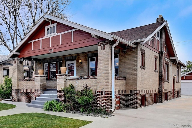 view of front facade with a porch, brick siding, a chimney, and a shingled roof