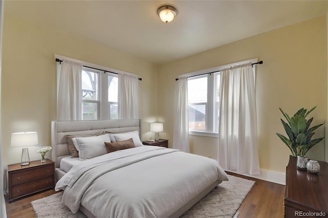 bedroom with multiple windows, dark wood-type flooring, and baseboards