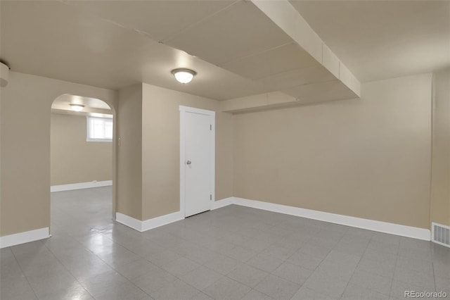basement with arched walkways, baseboards, and tile patterned flooring