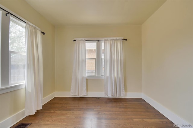 empty room featuring plenty of natural light, wood finished floors, and baseboards