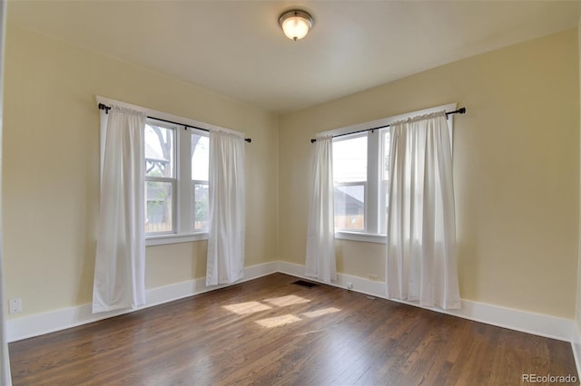 empty room with dark wood-style flooring, plenty of natural light, and baseboards