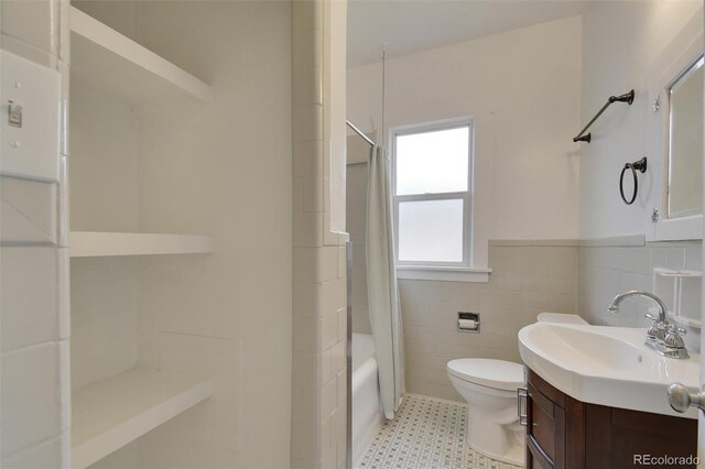 full bath with tile walls, toilet, vanity, shower / tub combo, and wainscoting