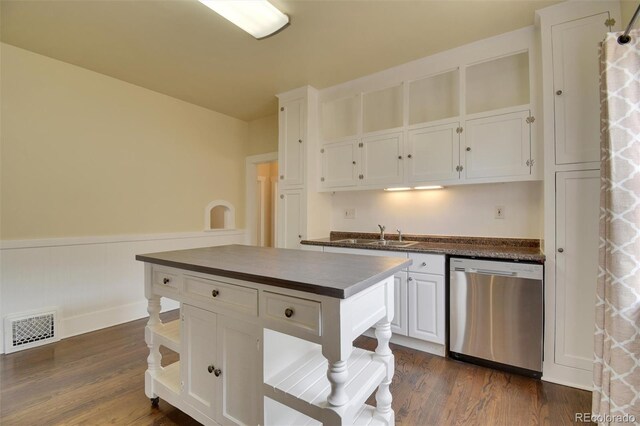 kitchen featuring stainless steel dishwasher, dark countertops, a sink, white cabinetry, and wainscoting