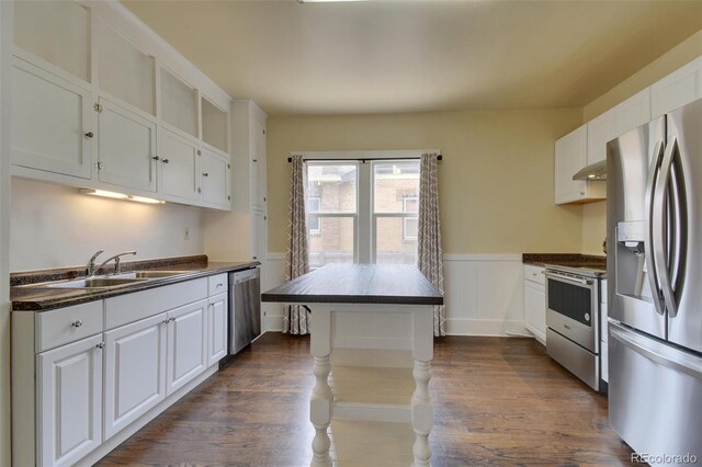 kitchen featuring appliances with stainless steel finishes, dark countertops, a wainscoted wall, white cabinets, and dark wood-type flooring