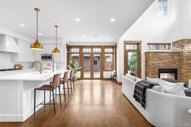 kitchen with a fireplace, stainless steel microwave, open floor plan, wood finished floors, and premium range hood