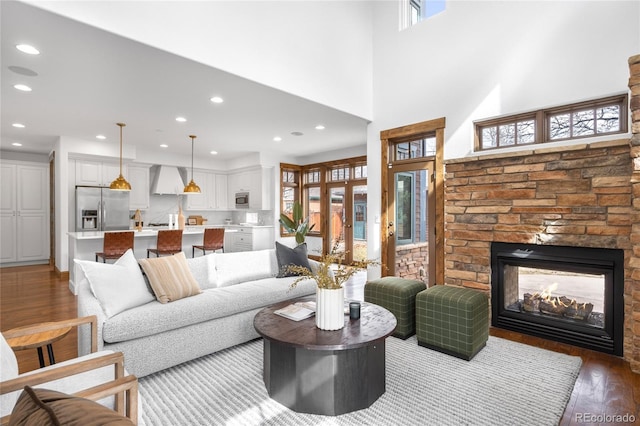 living area featuring a stone fireplace, wood finished floors, a towering ceiling, and recessed lighting