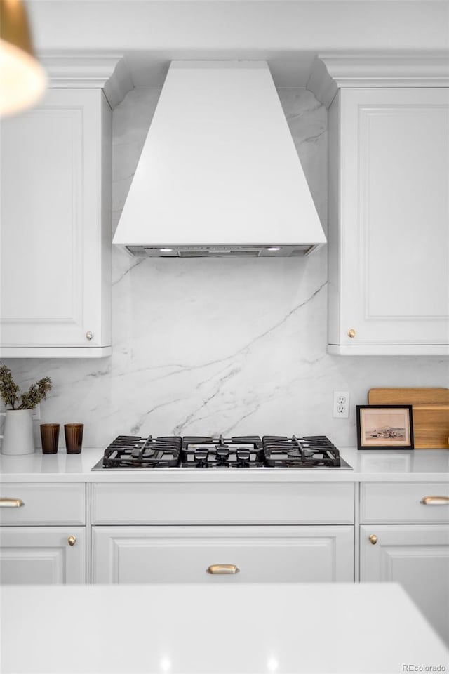 kitchen featuring light countertops, white cabinets, wall chimney range hood, and gas stovetop