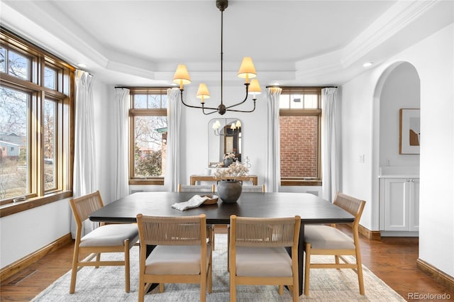 dining area featuring arched walkways, a raised ceiling, an inviting chandelier, and wood finished floors