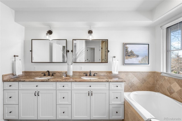 bathroom featuring double vanity, tiled bath, and a sink