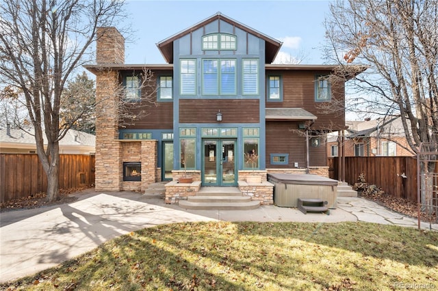 back of house with a chimney, french doors, fence, and a hot tub