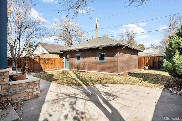 rear view of house with fence private yard, roof with shingles, and a patio