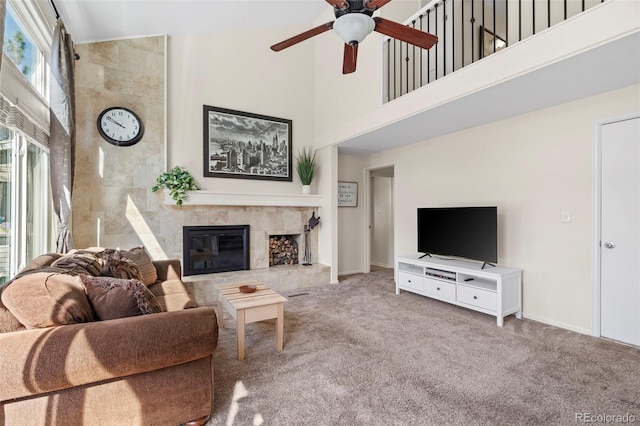 carpeted living room featuring a fireplace, baseboards, a towering ceiling, and ceiling fan