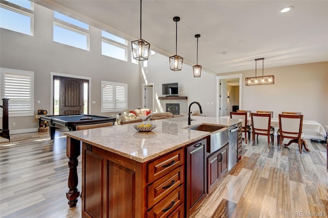 3308 County Road 19, Fort Lupton, CO 80621 - kitchen featuring a sink, a stone fireplace, light wood-style flooring, a kitchen island with sink, and pendant lighting