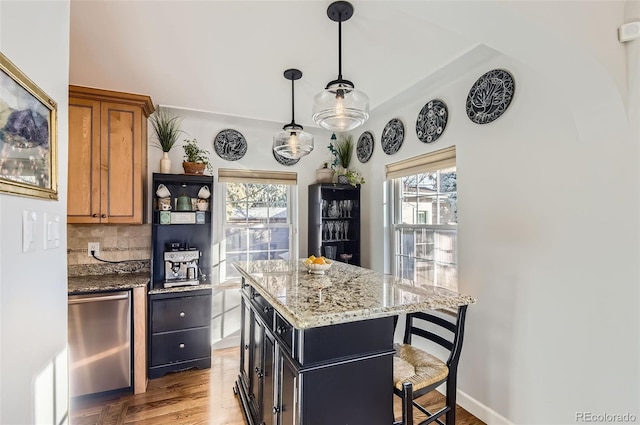 kitchen featuring a breakfast bar, light stone countertops, decorative backsplash, a kitchen island, and decorative light fixtures