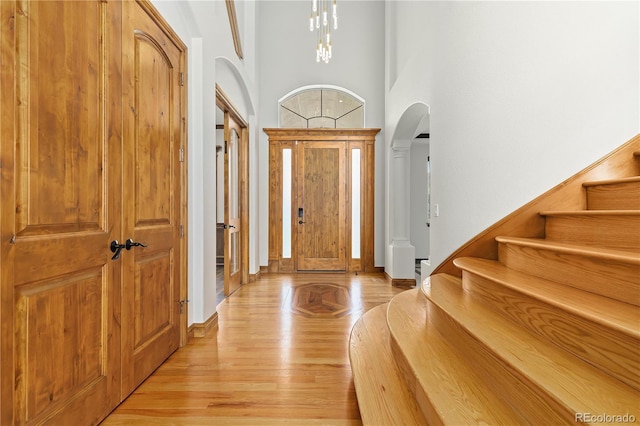 entryway featuring arched walkways, a high ceiling, an inviting chandelier, light wood-type flooring, and stairs