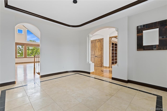 spare room with arched walkways, light tile patterned floors, a raised ceiling, and baseboards