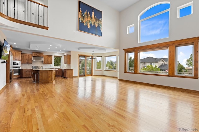 unfurnished living room featuring baseboards, a high ceiling, recessed lighting, and light wood-style floors