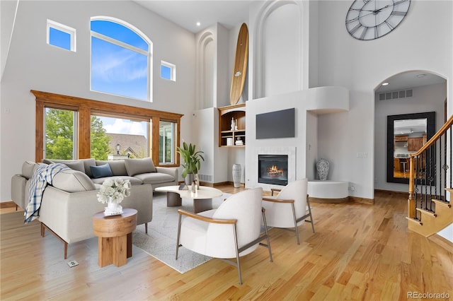 living area featuring visible vents, baseboards, stairs, light wood-style floors, and a glass covered fireplace