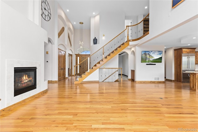 unfurnished living room with arched walkways, a fireplace, light wood finished floors, visible vents, and stairway