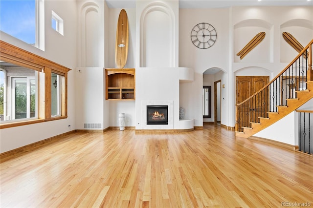 unfurnished living room featuring visible vents, stairway, a glass covered fireplace, wood finished floors, and baseboards