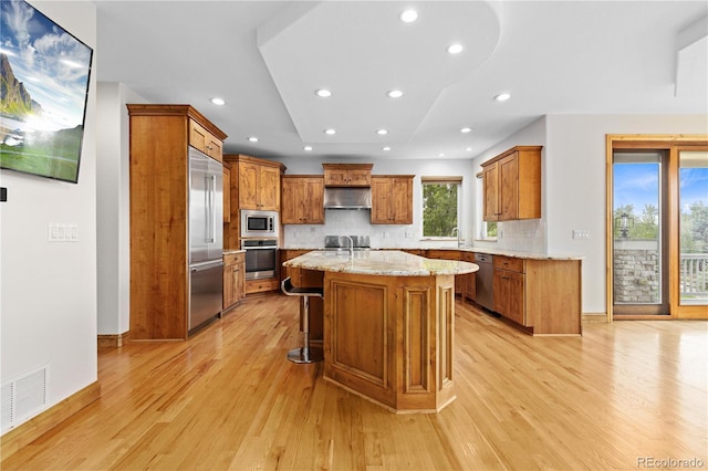 kitchen featuring light stone counters, a breakfast bar, a kitchen island, built in appliances, and under cabinet range hood