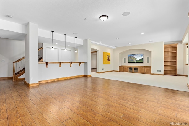 unfurnished living room with baseboards, stairs, light wood-style floors, built in shelves, and recessed lighting