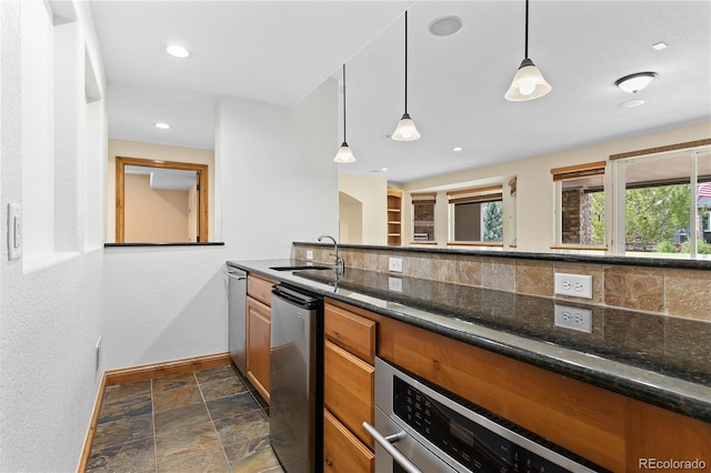 kitchen with decorative light fixtures, stone tile flooring, decorative backsplash, a sink, and dark stone countertops