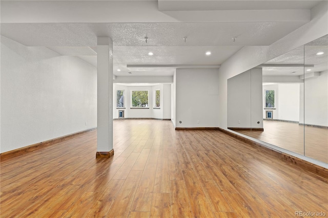 empty room featuring light wood-style floors, baseboards, a textured ceiling, and recessed lighting