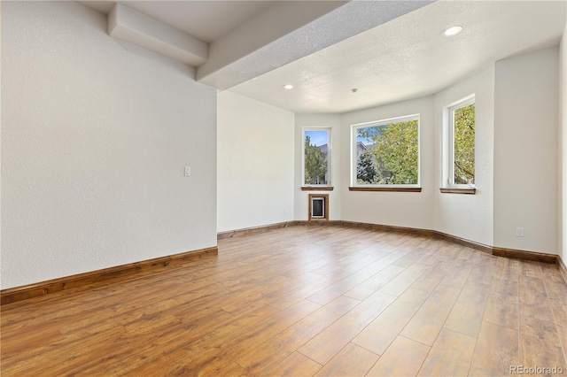 unfurnished room featuring light wood finished floors, baseboards, a textured ceiling, and recessed lighting