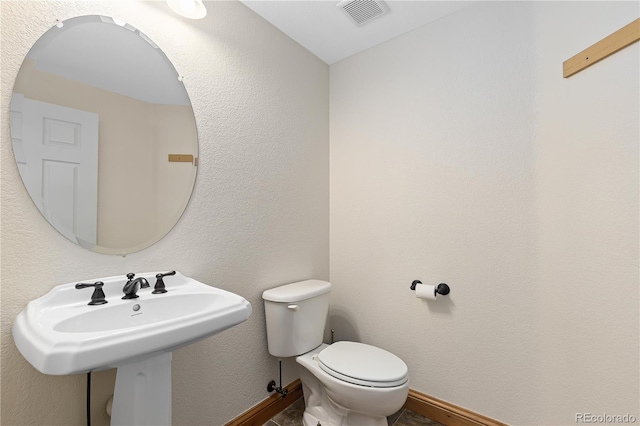 half bathroom with toilet, baseboards, visible vents, and a textured wall