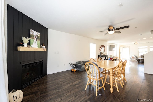 dining area featuring dark hardwood / wood-style flooring, ceiling fan, and a large fireplace