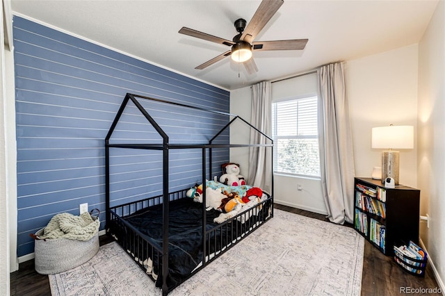 bedroom featuring ceiling fan, hardwood / wood-style floors, and wooden walls