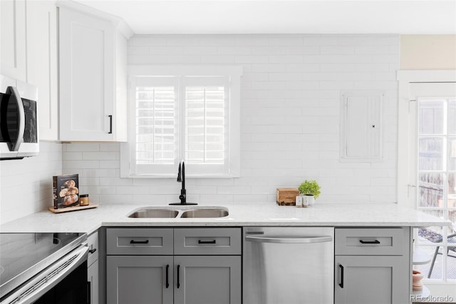 kitchen featuring stainless steel appliances, a sink, gray cabinets, a wealth of natural light, and backsplash