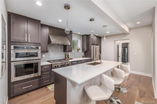 kitchen with sink, wall chimney exhaust hood, stainless steel appliances, an island with sink, and a breakfast bar