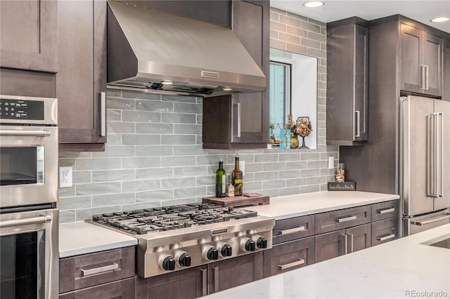 kitchen with decorative backsplash, appliances with stainless steel finishes, dark brown cabinets, and wall chimney range hood