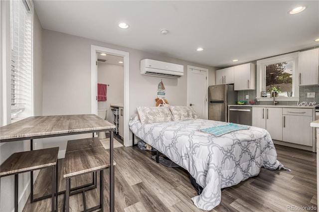 bedroom with a wall unit AC, stainless steel refrigerator, sink, and light hardwood / wood-style flooring