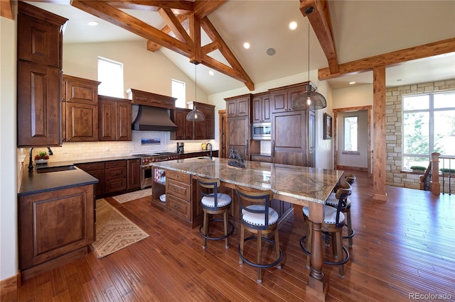 kitchen featuring high end appliances, a sink, a large island with sink, custom range hood, and dark wood finished floors