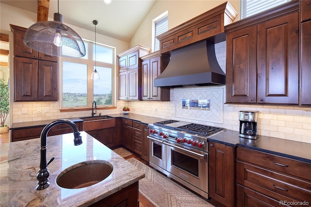 kitchen with double oven range, a sink, wall chimney exhaust hood, dark stone countertops, and vaulted ceiling
