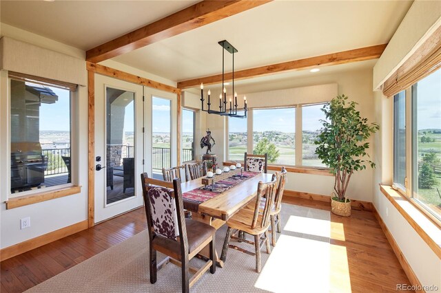 dining room featuring beamed ceiling, wood finished floors, a chandelier, baseboards, and a water view